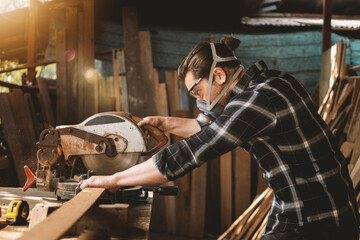 Carpenter wearing googles using a chop saw to cut wood plank on the table work with measure tape at...