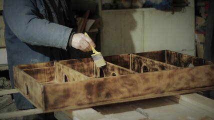 staining the surface of a wooden product with a protective liquid, staining an exclusive game of wood on a work table in a carpentry workshop, creating unique products from handmade wood