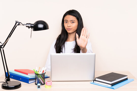 Student asian girl in a workplace with a laptop isolated on beige background making stop gesture