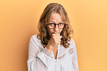 Middle age blonde woman wearing casual clothes over yellow background feeling unwell and coughing as symptom for cold or bronchitis. health care concept.