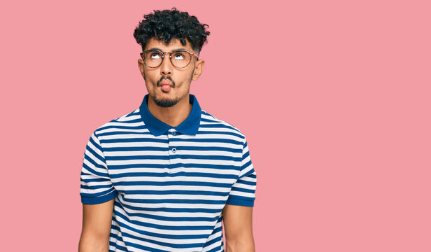 Young arab man wearing casual clothes and glasses making fish face with lips, crazy and comical gesture. funny expression.