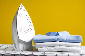 Steam blue iron on ironing board. Yellow background. Clothes, ironing board household concept.