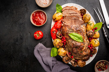 Baked pork meat with grilled vegetables on a plate on dark background, top view
