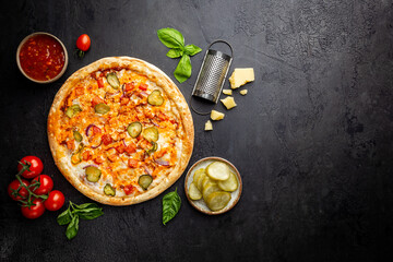 Tasty cheeseburger pizza and cooking ingredients tomatoes and basil on dark background. Top view