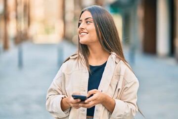 Fototapeta premium Young hispanic girl smiling happy using smartphone at the city.
