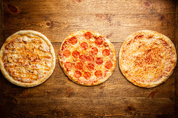 Flat-lay of different types of pizza and red wine over rustic wooden table, top view. Fast food lunch, celebration, pizza party
