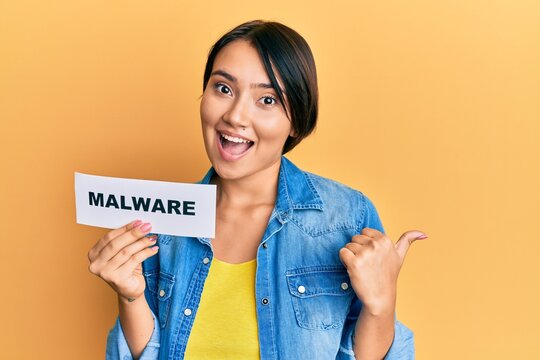 Beautiful young woman with short hair holding malware paper pointing thumb up to the side smiling happy with open mouth