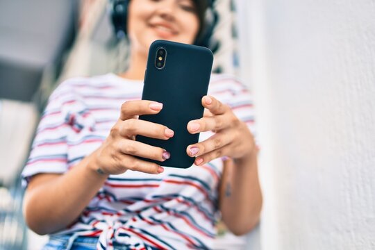 Young latin girl smiling happy using smartphone and headphones at the city