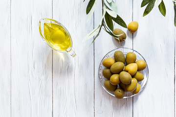 Olive oil and bowl of green olives on a white wooden table. Modern minimal still life, glass bowl...