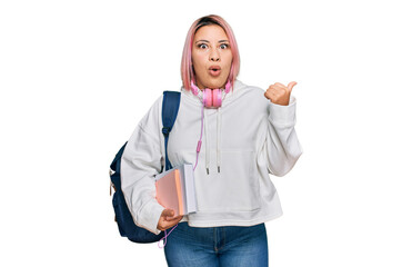 Hispanic woman with pink hair wearing student backpack and headphones surprised pointing with hand...