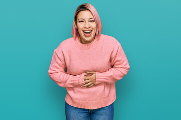 Hispanic woman with pink hair wearing casual winter sweater smiling and laughing hard out loud...