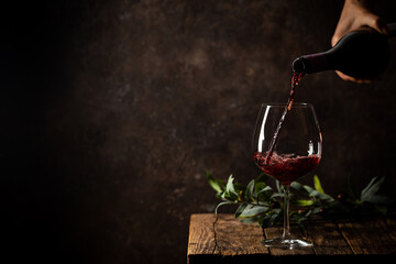 Fototapeta premium Pouring red wine into the glass against rustic dark wooden background