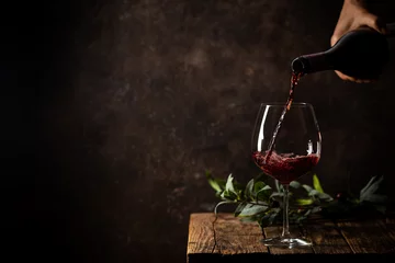 Fototapeten Pouring red wine into the glass against rustic dark wooden background © petrrgoskov