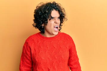 Fototapeta na wymiar Young hispanic woman with curly hair wearing casual winter sweater angry and mad screaming frustrated and furious, shouting with anger. rage and aggressive concept.