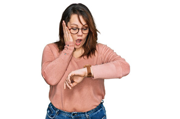 Young plus size woman wearing casual clothes and glasses looking at the watch time worried, afraid...