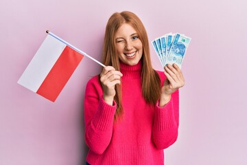 Young irish woman holding poland flag and zloty banknotes winking looking at the camera with sexy expression, cheerful and happy face.