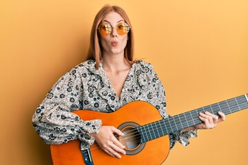 Young irish woman wearing boho style playing classical guitar looking at the camera blowing a kiss being lovely and sexy. love expression.