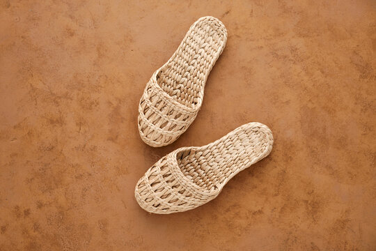 Comfortable and stylish home or beach slippers made of natural tropical rattan. Brown background. View from above. Safe for the environment. Zero waste and sustainable free lifestyle. 