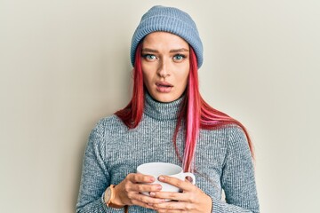 Young caucasian woman wearing winter cap and drinking a cup of hot coffee clueless and confused...