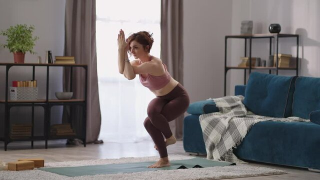 hatha yoga training at home, woman is standing in garudasana, lady is performing eagle position, workout for balance, keeping fit