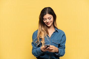Young Russian girl isolated on yellow background sending a message with the mobile
