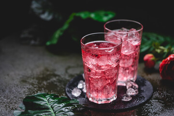 Red drink cocktail or lemonade with ice in a glass on dark background.