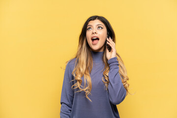 Young Russian girl using mobile phone isolated on yellow background laughing