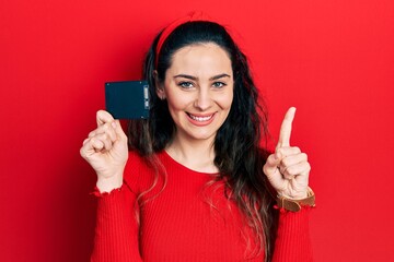 Young hispanic woman holding ssd memory smiling with an idea or question pointing finger with happy face, number one