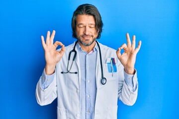 Middle age handsome man wearing doctor uniform and stethoscope relax and smiling with eyes closed doing meditation gesture with fingers. yoga concept.