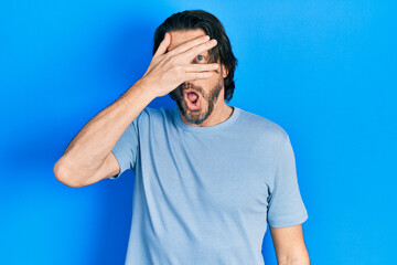 Middle age caucasian man wearing casual clothes peeking in shock covering face and eyes with hand, looking through fingers with embarrassed expression.