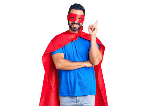 Young hispanic man wearing super hero costume smiling happy pointing with hand and finger to the side