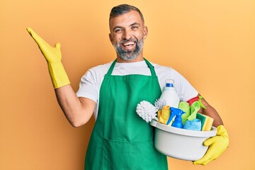 Middle age handsome man holding cleaning products celebrating victory with happy smile and winner...