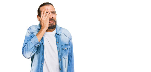 Attractive man with long hair and beard wearing casual denim jacket yawning tired covering half face, eye and mouth with hand. face hurts in pain.