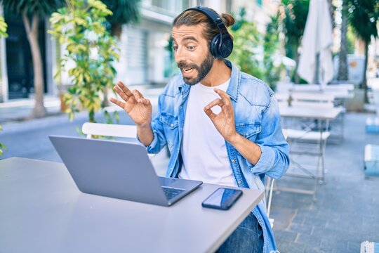 Young middle eastern man doing video call using laptop and headphones at coffee shop terrace.