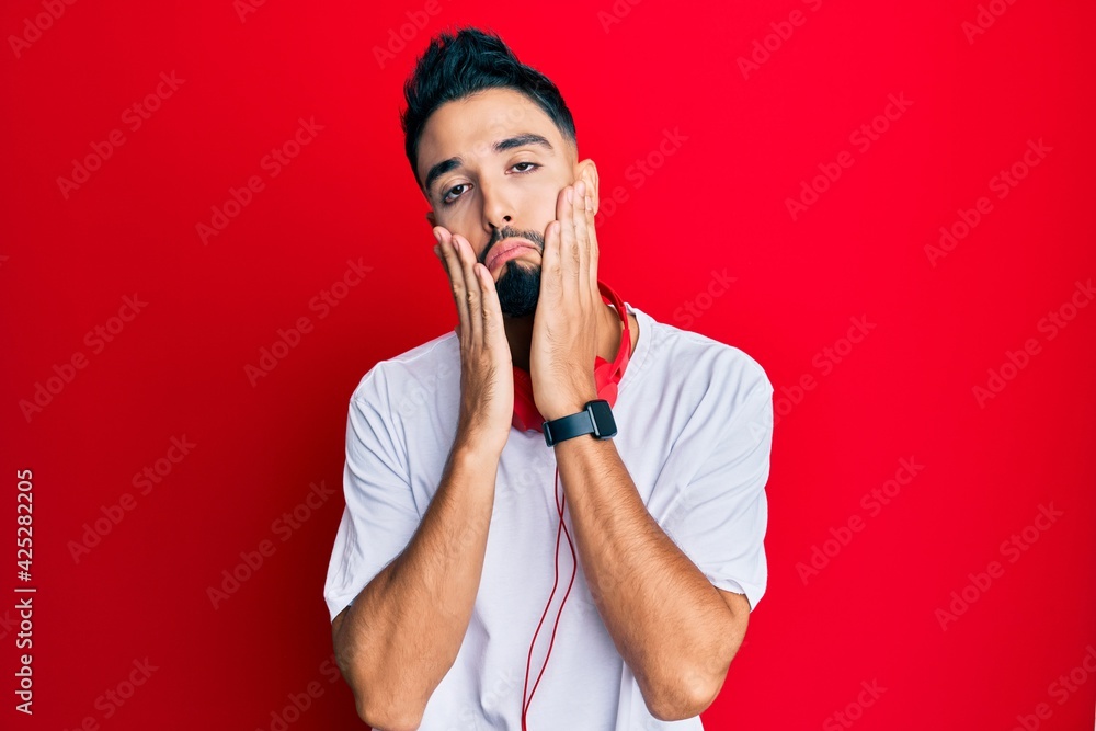 Wall mural young man with beard listening to music using headphones tired hands covering face, depression and s