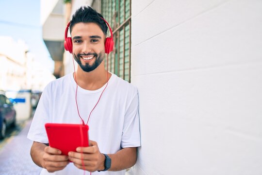 Young arab man smiling happy using headphones and touchpad at the city.