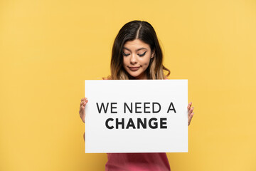 Young Russian girl isolated on yellow background holding a placard with text We Need a Change