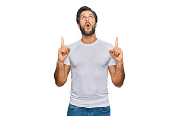 Fototapeta premium Young hispanic man wearing casual white t shirt amazed and surprised looking up and pointing with fingers and raised arms.
