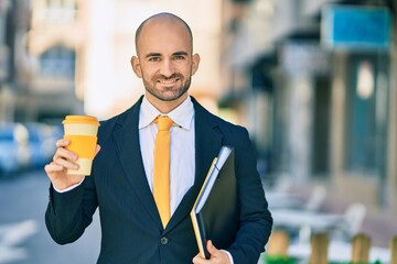 Young hispanic bald businessman holding binder drinking coffee at the city.