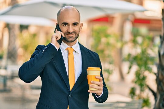 Young hispanic bald businessman talking on the smartphone drinking coffee at the city.