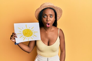 Young african woman holding sun draw scared and amazed with open mouth for surprise, disbelief face