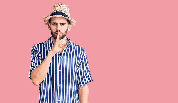 Young handsome man with beard wearing summer hat and striped shirt asking to be quiet with finger on lips. silence and secret concept.