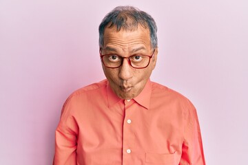 Middle age indian man wearing casual clothes and glasses making fish face with lips, crazy and comical gesture. funny expression.