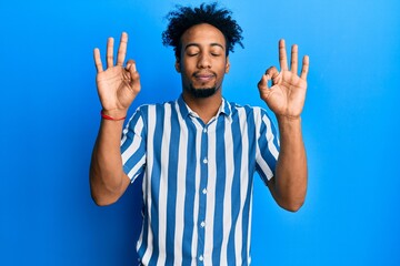 Young african american man with beard wearing casual striped shirt relax and smiling with eyes closed doing meditation gesture with fingers. yoga concept.