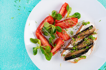 Sandwich - smorrebrod with sprats and tomatoes salad on white plate. Danish cuisine.  Eco friendly concept. Top view, flat lay