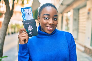 Young african american woman smiling happy holding usa passport and boarding pass at the city.