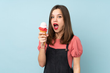 Teenager girl holding a cornet ice cream isolated on blue background with surprise and shocked...