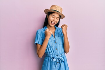 Young chinese woman wearing summer hat celebrating surprised and amazed for success with arms raised and eyes closed