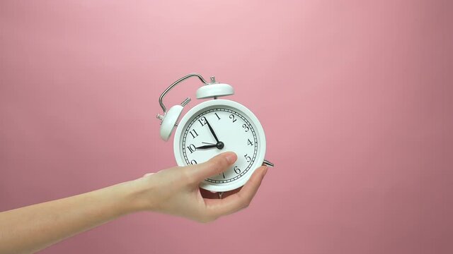 Close Up of hand holding alarm clock on pink background.