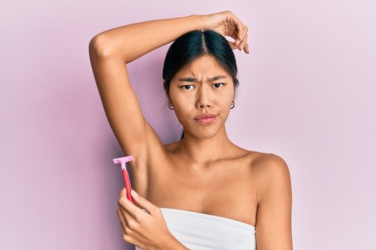 Young chinese woman wearing shower towel using razor skeptic and nervous, frowning upset because of problem. negative person.